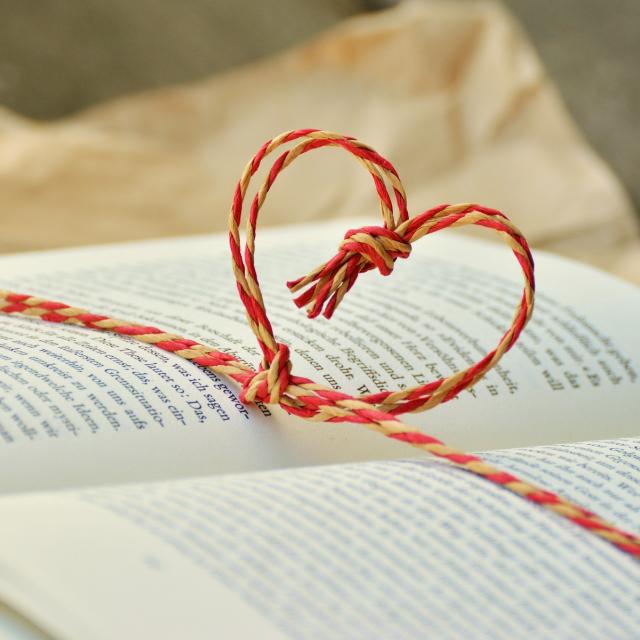 Stimmungsbild zum Beitrag: Ein aufgeschlagenes Buch, um das ein Band mit Herzform geknüpft ist, wird abgebildet.