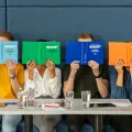 Stimmungsbild zum Beitrag: Es werden vier sitzende Personen abgebildet, die ihre Gesichter mit Steuergesetzbüchern bedecken.