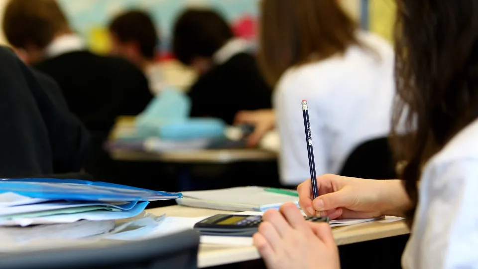 Stimmungsbild zum Beitrag: Es wird eine Frau an einem Schreibtisch in einer Klasse abgebildet.