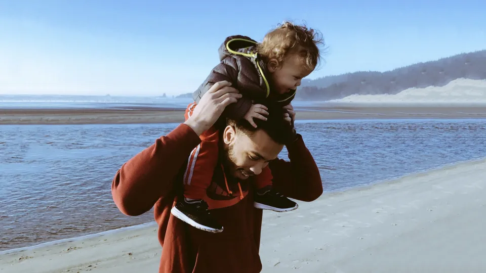 Stimmungsbild zum Beitrag: Es wird ein Vater, der sein Kind auf den Schultern trägt, abgebildet.