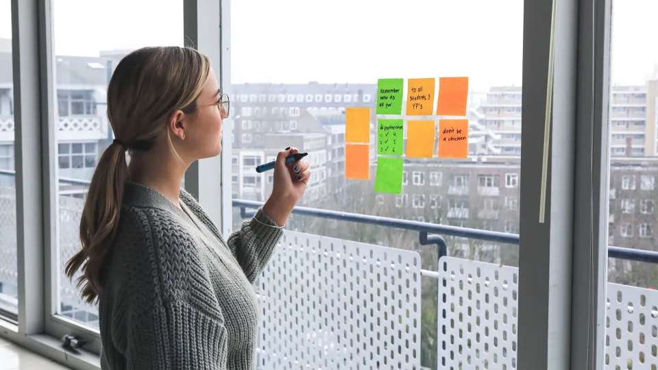 Stimmungsbild zum Beitrag: Es wird eine Frau am Fenster, die Notizen auf Post-its macht, abgebildet.