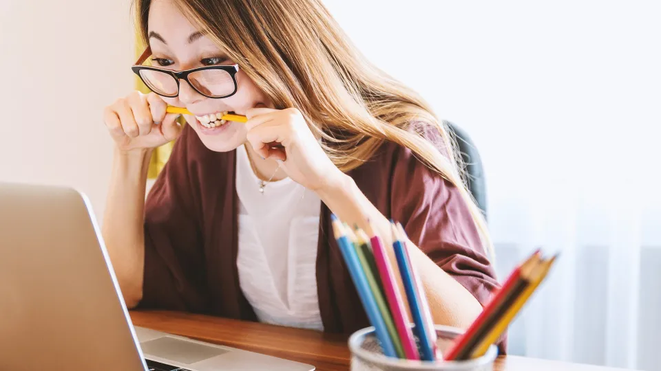 Stimmungsbild zum Beitrag: Es wird eine vor einem Laptop sitzende Frau mit einem Stift im Mund abgebildet.