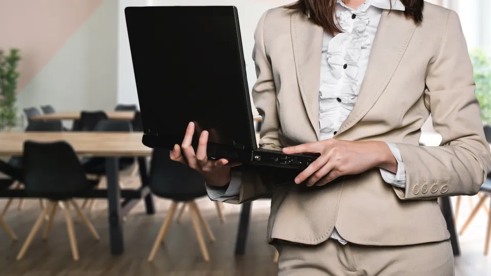 Stimmungsbild zum Beitrag: Es wird eine Frau im Hosenanzug mit Laptop in der Hand abgebildet.