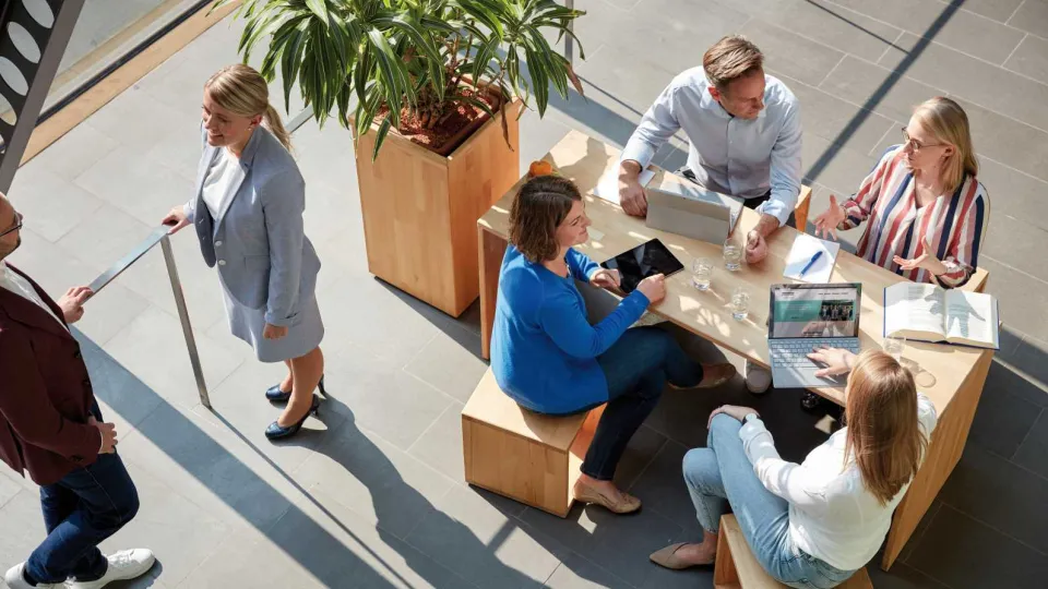 Stimmungsbild zur Startseite: Es werden Menschen sitzend an einem Tisch im Foyer abgebildet.